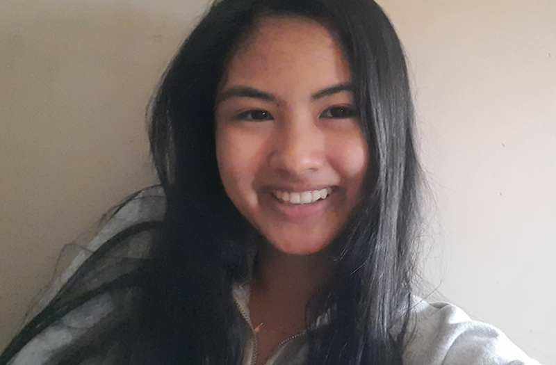 Smiling woman with long black hair wearing a light gray top, posing indoors.